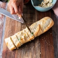 A hand using a spreading knife to spread the garlic butter in between the slices of bread and on the top as well covering it well and