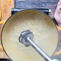 An immersion blender being used to puree the soup for those who like a smooth broccoli and cheddar soup recipe