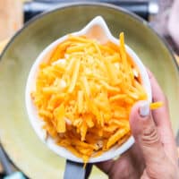 A hand holding in a bowl of shredded cheese ready to add them in to the soup