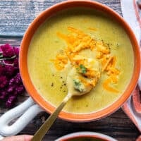 A hand spooning some broccoli cheddar soup in a bowl showing the chunks of broccoli and the silky creamy smooth soup