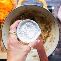 A hand holding the flour to add to the pot to make the roux in order to thicken the broccoli cheddar soup