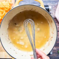 A hand holding a whisk to dissolve the roux into the stock