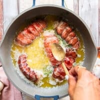 A spoon drenching the tops of the lobster tails with the butter sauce to help it cook the way through