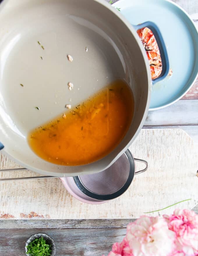 The butter sauce being poured over a sieve over a bowl to strain 