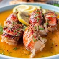 close up of a butter poached lobster showing the oink lobster and the golden flavored butter around it surrounded by lemon slices