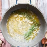 Crushed garlic cloves and fresh herbs are added to the melted butter in the skillet