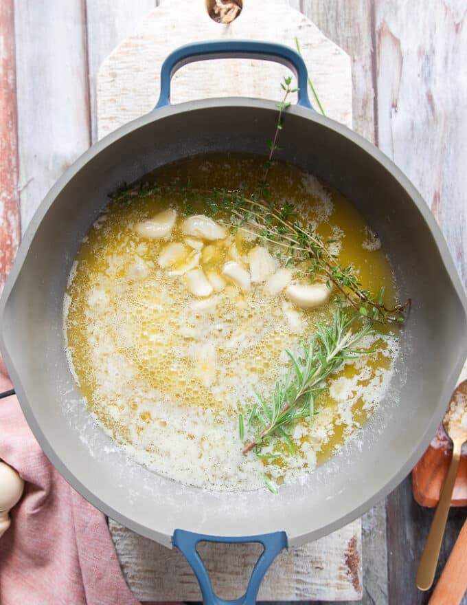 Crushed garlic cloves and fresh herbs are added to the melted butter in the skillet