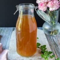 Lobster stock in a large jar showing the beautiful clear color of the stock and a some oregano around it