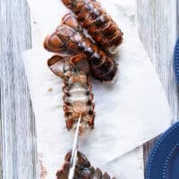 A hand holding a scissors and cutting through the back of the lobster to cut it open