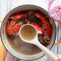 A ladle placed in the post of lobster stock showing how golden and rich the color of the stock is so it's ready
