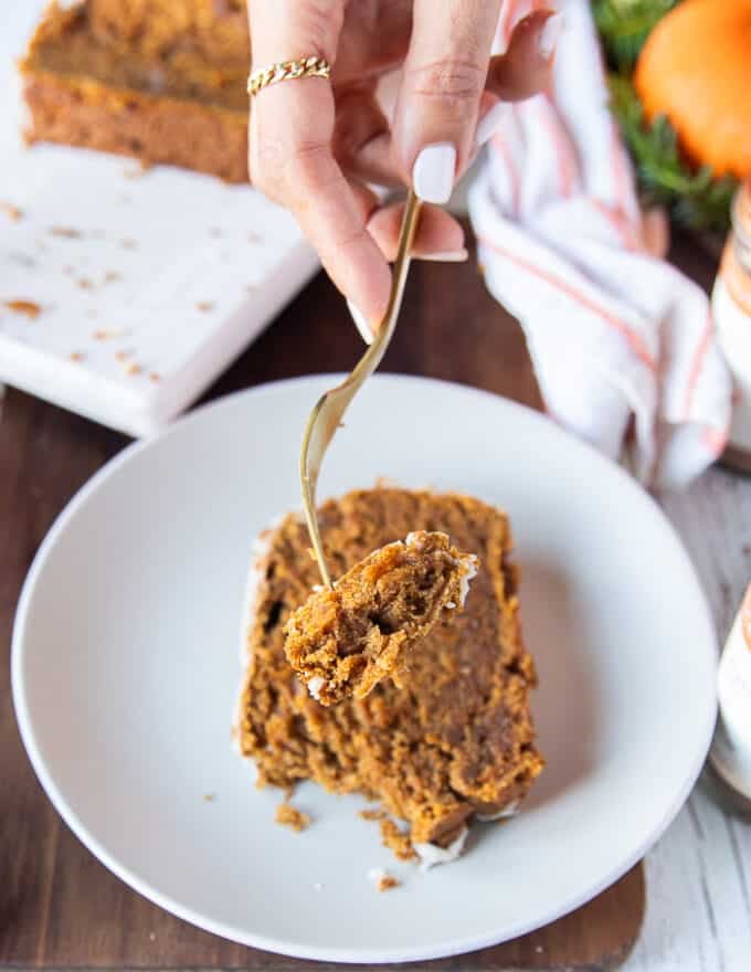 A hand holding a fork with a chunk of pumpkin bread showing close up the texture and how soft and moist the bread is. 