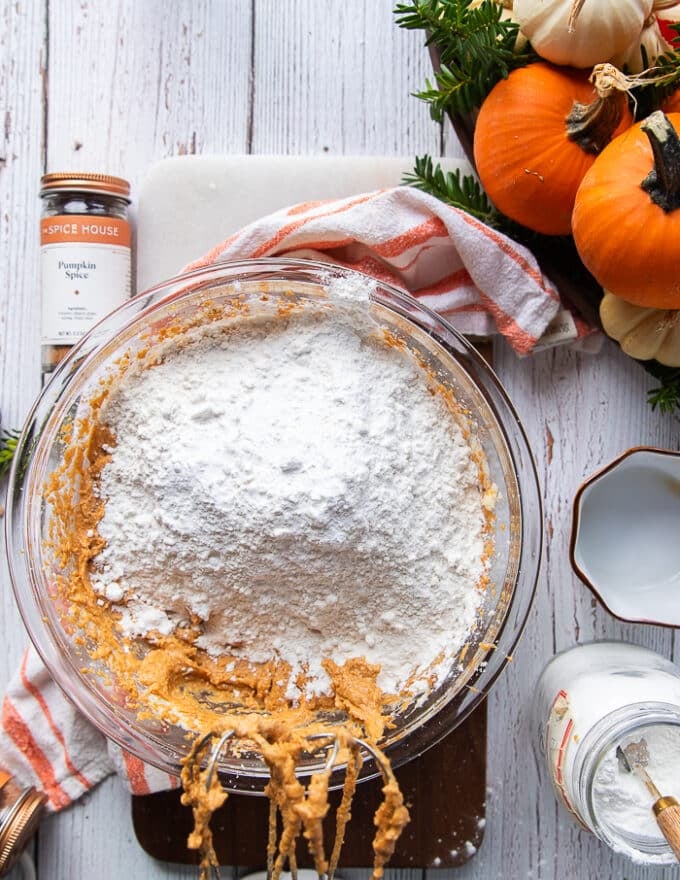 The flour, baking soda and baking powder are added on to the pumpkin bread batter now and a spatula is used to incorporate them 