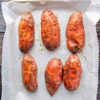 seasoned cut sweet potatoes placed on a parchment lined baking sheet, cut side down