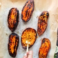A hand holding a fork and smashing the inside of the sweet potatoes to prepare them for stuffing