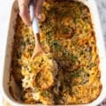 A hand using a large spoon to scoop up some tuna casserole showing the texture of the noodles and tuna and the crunchy topping