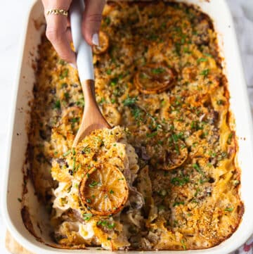 A hand using a large spoon to scoop up some tuna casserole showing the texture of the noodles and tuna and the crunchy topping