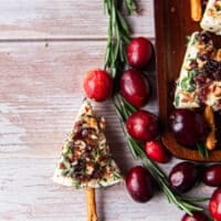 Close up of one cheese tree on a board with a sprig of rosemary and fresh cranberries