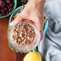 A hand holding a mini processor bowl showing the pecans processed into bite size