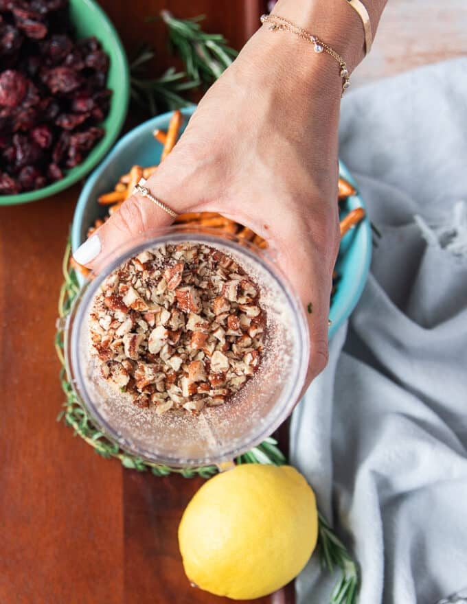 A hand holding a mini processor bowl showing the pecans processed into bite size