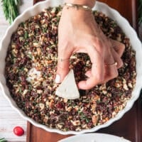 A hand taking a cheese wedge and pressing it down over the seasoning mixture so it sticks on the cheese