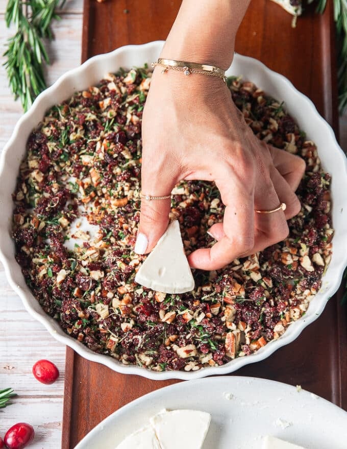 A hand taking a cheese wedge and pressing it down over the seasoning mixture so it sticks on the cheese