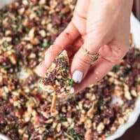 A hand holding a pretzel stick and inserting it at the base of the cheese to create the tree shape