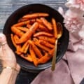 A hand holding a plate of Honey Roasted carrots ready, sweet and glazed with honey
