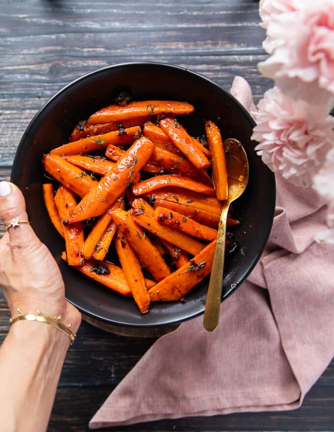 A hand holding a plate of Honey Roasted carrots ready, sweet and glazed with honey 
