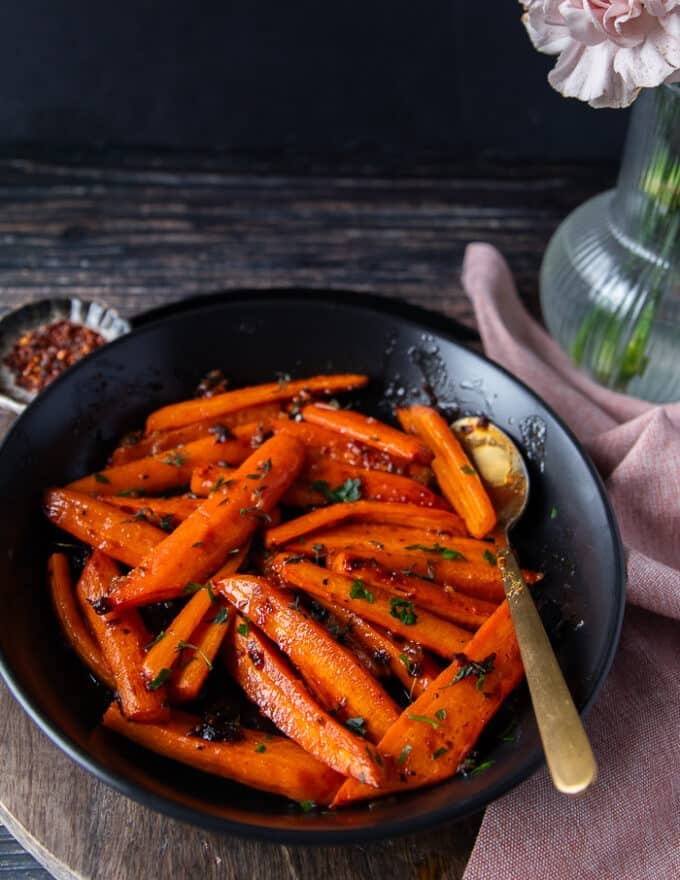 side view of a plate of honey roasted carrots with a serving spoon