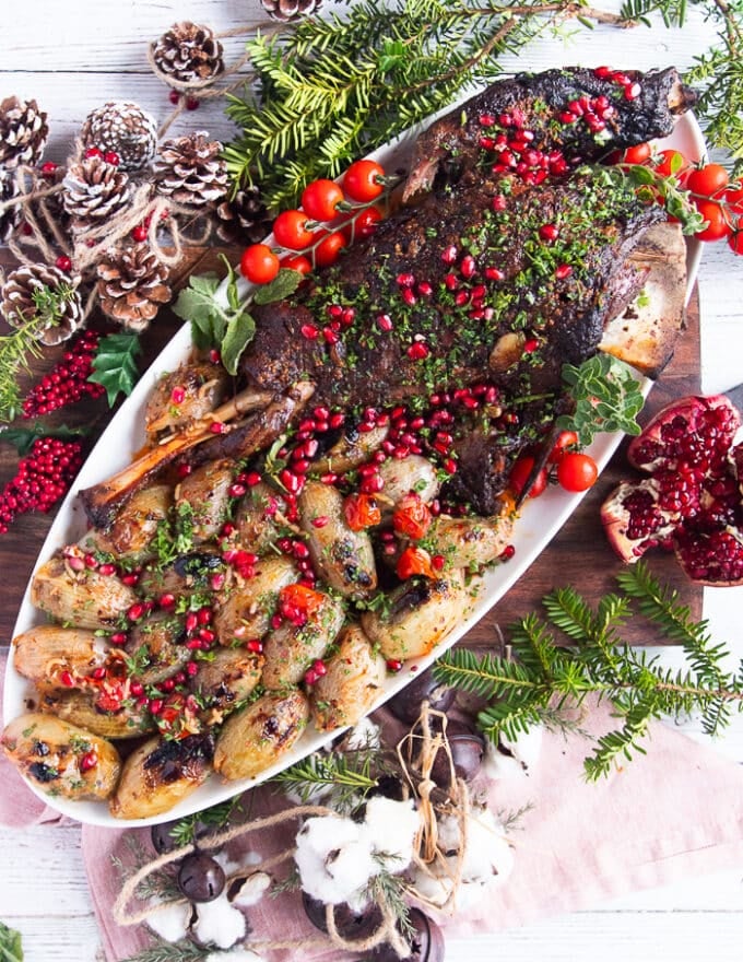 Holiday plate of lamb shoulder roast with stuffed onions around it and some holiday decorations on the table 