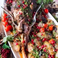 A fork flaking out the tender lamb shoulder roast showing how soft it is on a plate with some stuffed onions