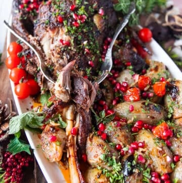A fork flaking out the tender lamb shoulder roast showing how soft it is on a plate with some stuffed onions