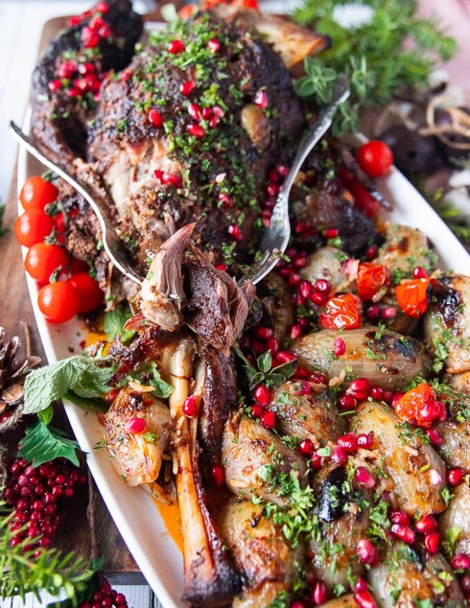 A fork flaking out the tender lamb shoulder roast showing how soft it is on a plate with some stuffed onions