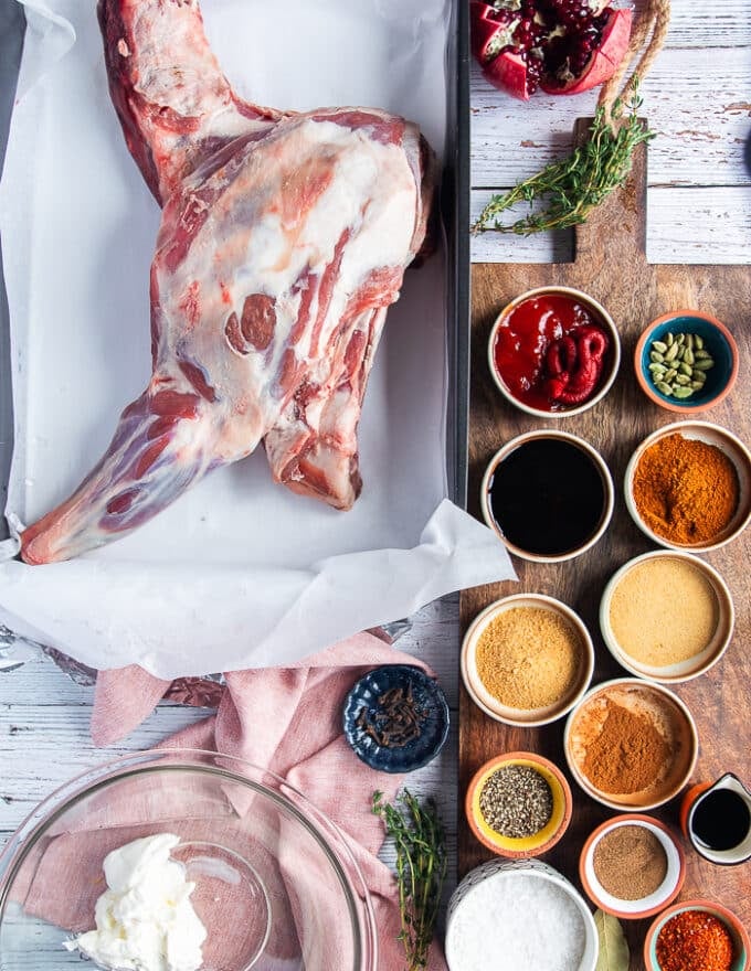 The marinade for the lamb shoulder roast including yogurt in a bowl, some pomegranate molasses in a bowl, lots of dry spices, olive oil, some ketchup and some fresh herbs and whole spices 
