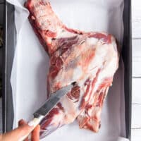 A hand making slits along the lamb shoulder using a small knife