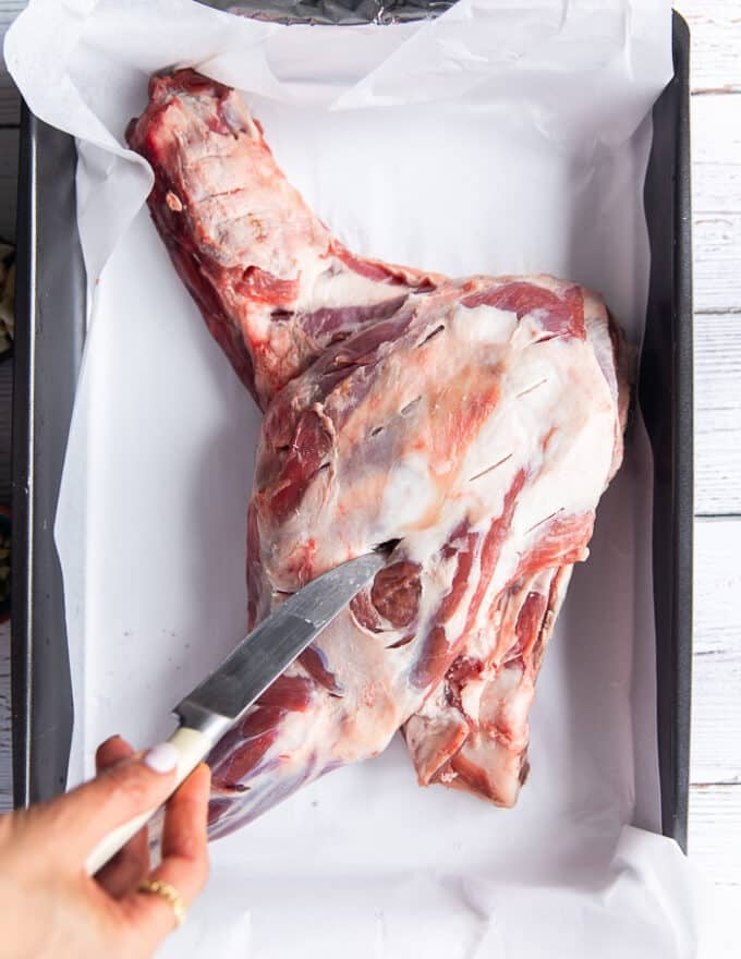 A hand making slits along the lamb shoulder using a small knife 