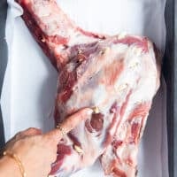 A hand inserting whole garlic cloves into the slits along the lamb shoulder