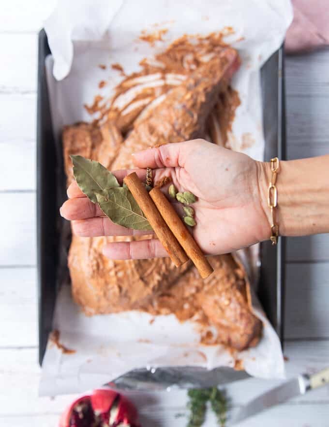 A hand holding whole spices like cinnamon sticks, bay leaves and cardamom pods