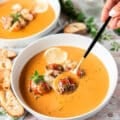 A hand holding a spoonful of lobster bisque close up to the camera showing succulent lobster in a creamy bisque