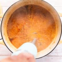 A hand using an immersion blender to blend the smooth into a silky smooth bisque