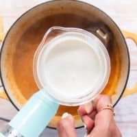 Some cream in a cup being poured into the pot of lobster bisque for a silky creamy finish