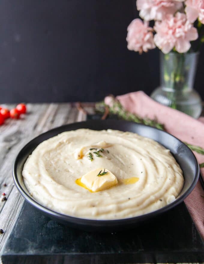 close up of the mashed potatoes served on a plate with a teaspoon of butter on top melting away. 