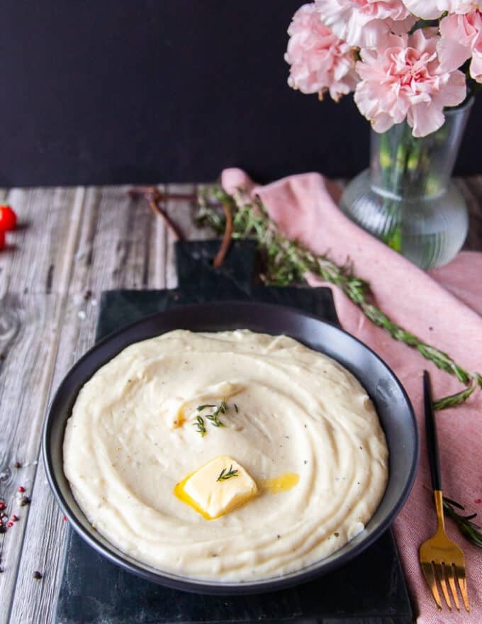 Side view of a plate of perfect mashed potatoes recipe with a dab of butter melting on top, some fresh thyme leaves and cracked black pepper 