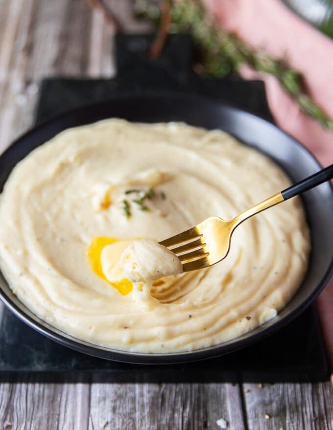 A fork spooning out some of the mashed potatoes with the melted butter on top showing the creamy texture.