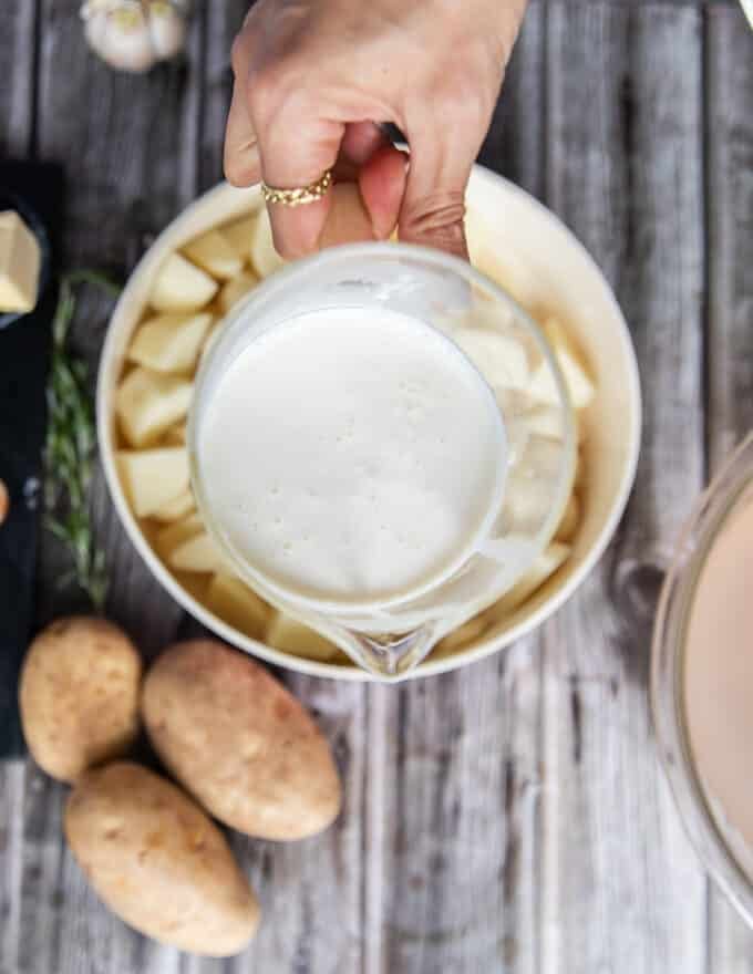 A hand holding a jar of milk and cream mixed together ready to boil in the potatoes with for a creamier mashed potatoes recipes