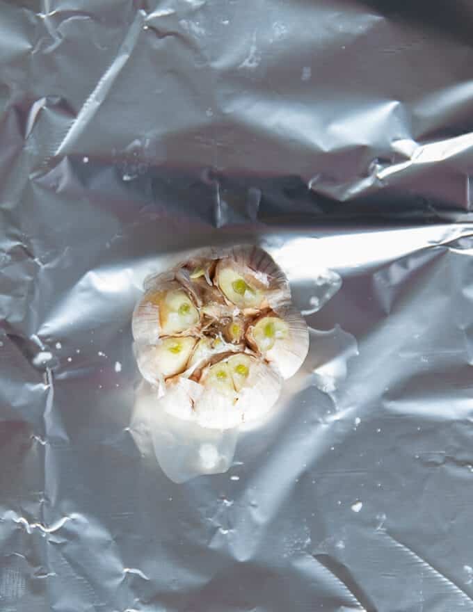 a head of garlic with the tops cut off in the middle of some foil. Drizzled with olive oil and sea salt