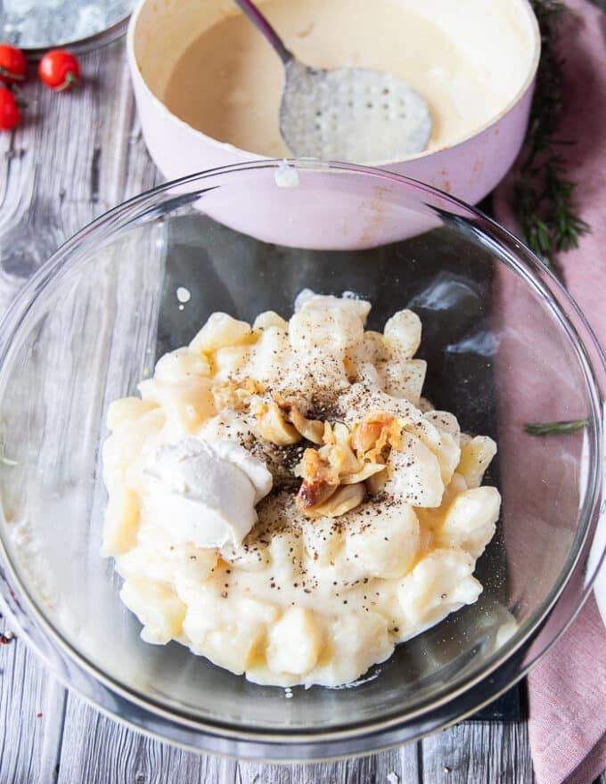 a large bowl with the boiled potatoes, the roasted garlic cloves on top, some butter, seasoning and some cream cheese