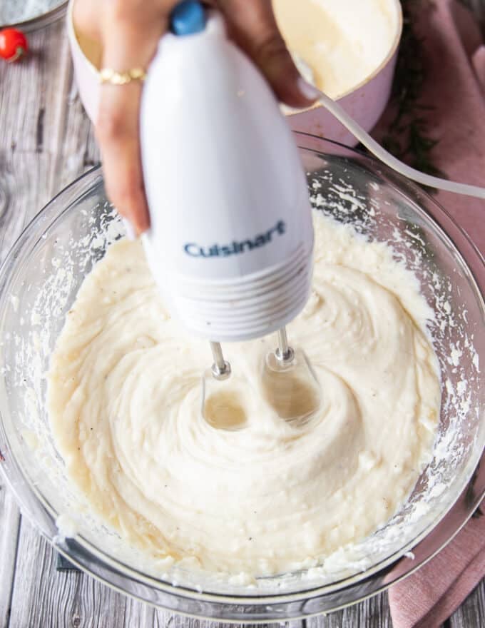 A hand holding a hand mixer and using it to fluff up the potatoes and mash them instead of a potato masher 