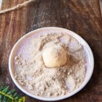 The cookie sough ball being rolled in vanilla sugar in a plate of vanilla sugar