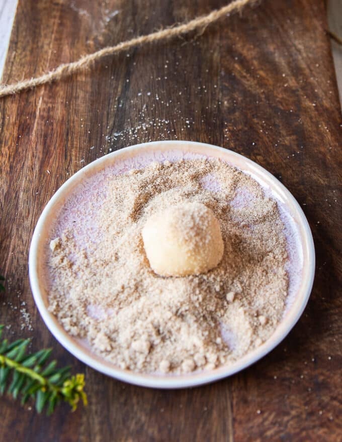 The cookie sough ball being rolled in vanilla sugar in a plate of vanilla sugar 